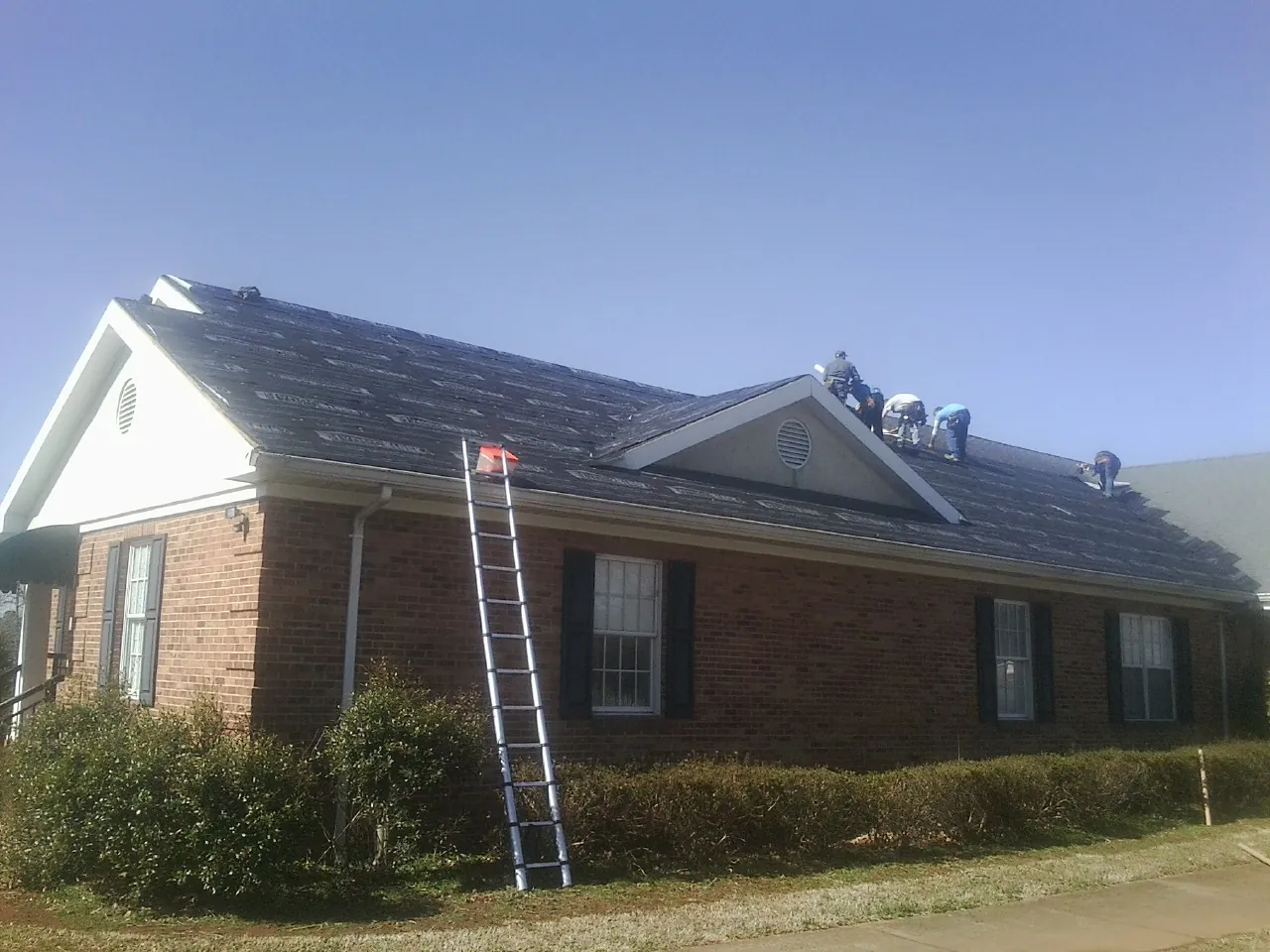 Crew tearing shingles off a brick ranch roof with a ladder set — Emergency Roof Repair work by our crew in Fort Monroe
