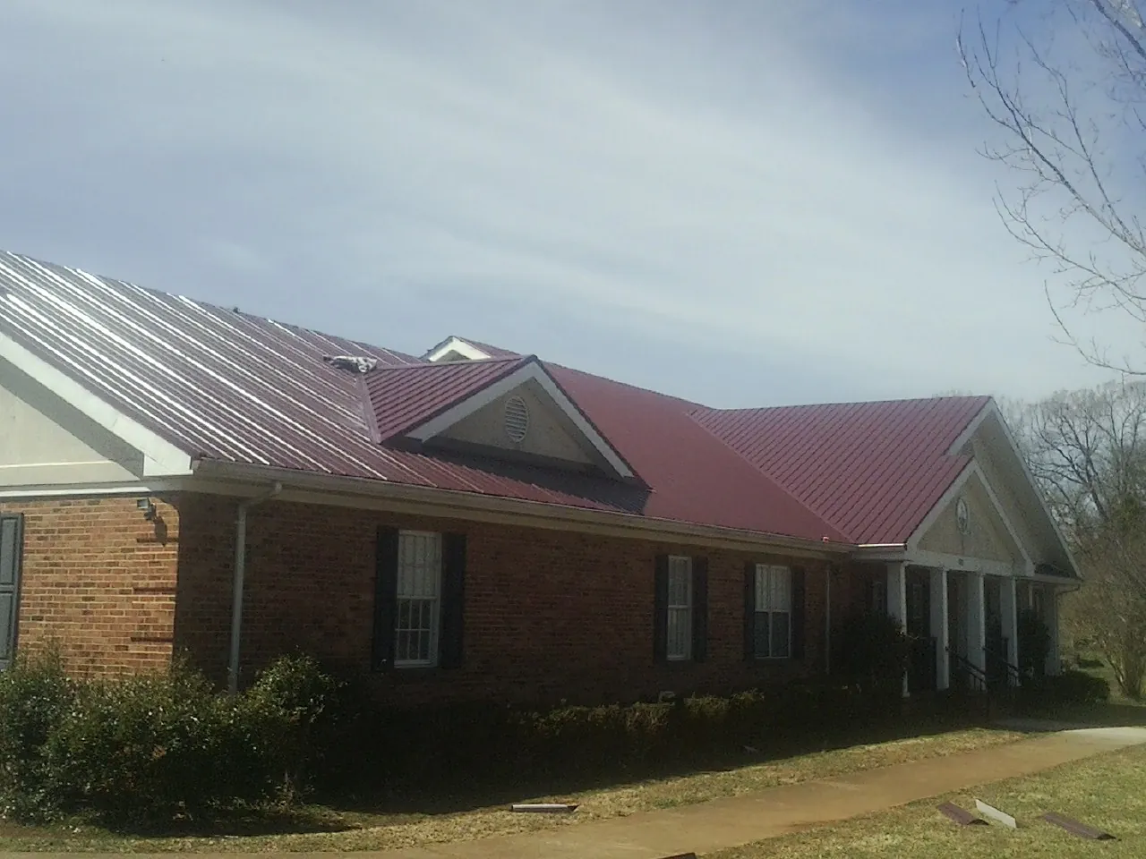 Red metal roof with gabled entries on a long brick building, from a Hail Damage Roof Repair job in Fort Monroe