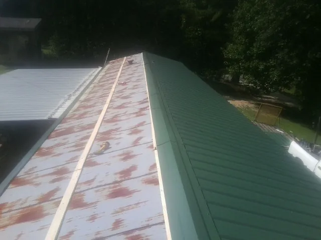 Old rusted panels beside newly installed green metal roofing — Wind Damage Roof Repair by Roofing Brothers in Fort Monroe