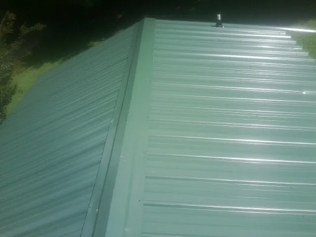 New green metal panels meeting at the ridge of a roof — Flat Roof Repair work by our crew in Fort Monroe