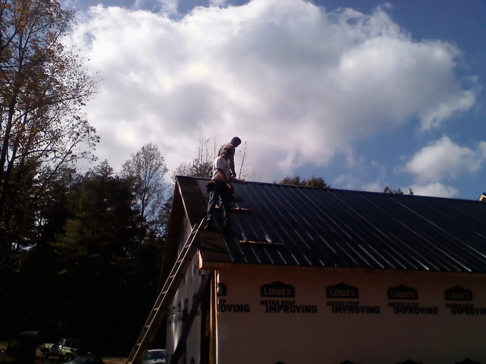 Roofer fastening dark metal panels high against a cloudy sky, from a Roof Inspection job in Fort Monroe