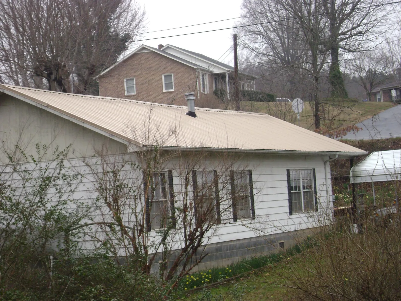 Tan metal roof on a white sided house set into a hillside — Commercial Roofing by Roofing Brothers in Fort Monroe